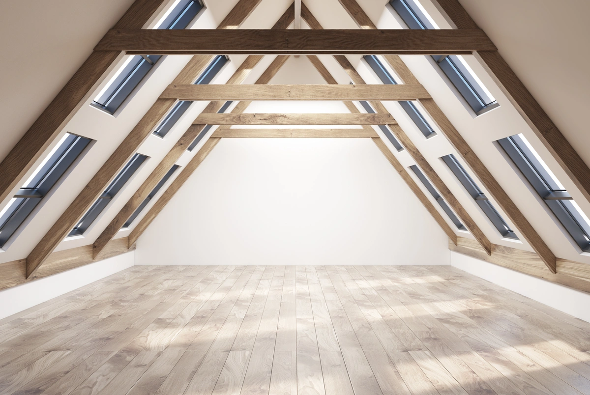 A modern, empty attic with wooden beams, light wood flooring, and multiple skylight windows on both sides.