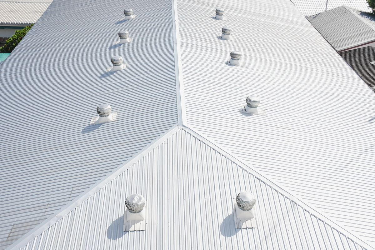 A white metal roof with multiple turbine vents evenly spaced along the ridge and slopes, photographed from above.