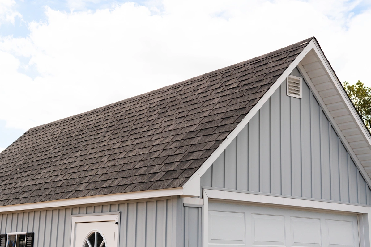 A close-up view of a house with light blue vertical siding, a gray shingled roof, a white garage door, and a white front door.