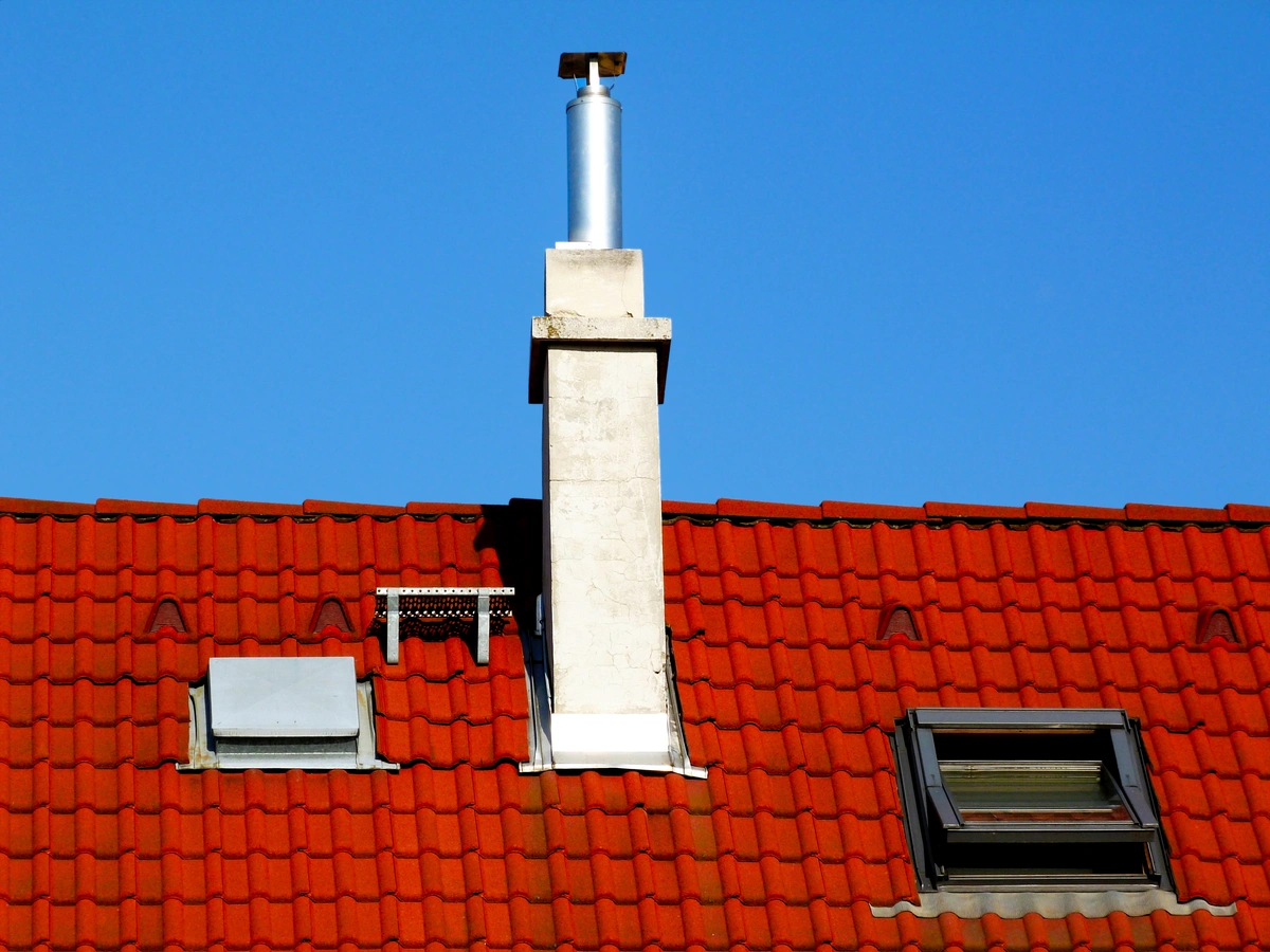 A white chimney and two skylights on a red tiled roof, set against a clear blue sky.