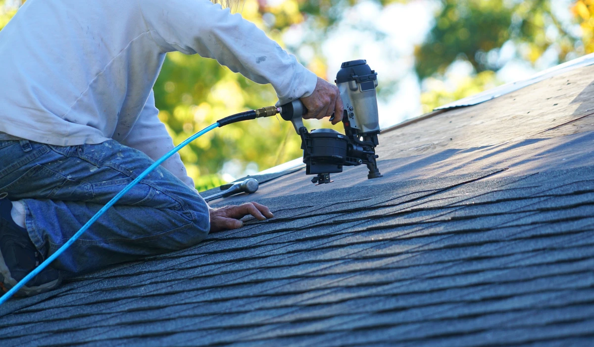 close up to worker using nail gun to install shingle