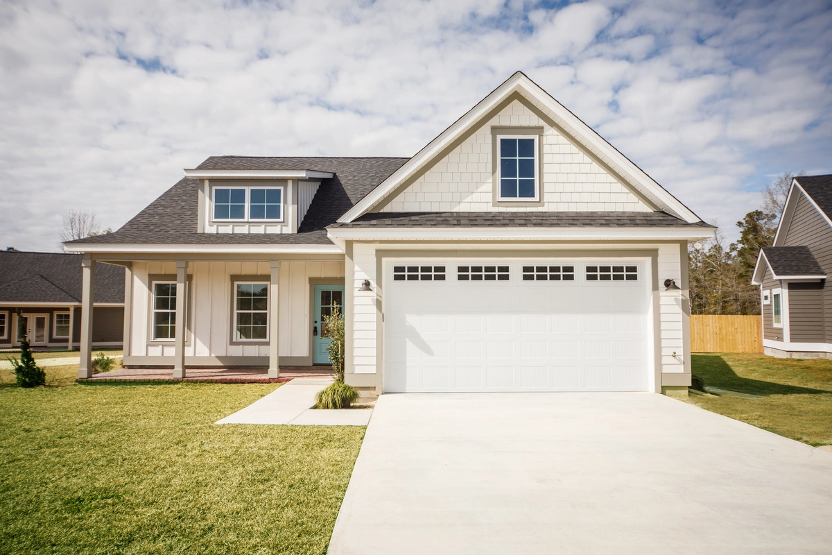 A modern suburban house with a double garage, covered front porch, and well-kept lawn under a partly cloudy sky.