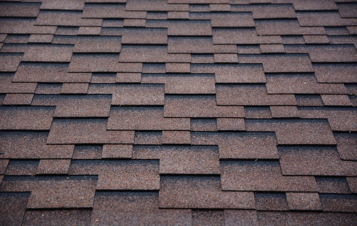 Close-up view of a roof covered with overlapping brown asphalt shingles arranged in a staggered pattern.