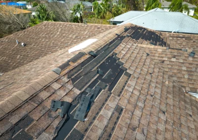 A house roof with missing and damaged shingles, exposing the black underlayment along the ridge, likely due to storm or wind damage.